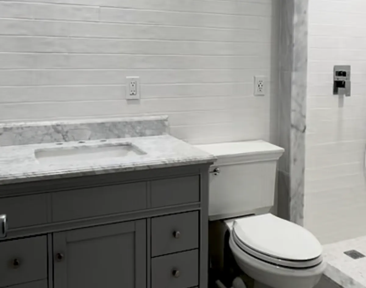 Remodeled bathroom with a gray vanity, marble countertop, new toilet and white subway tile walls