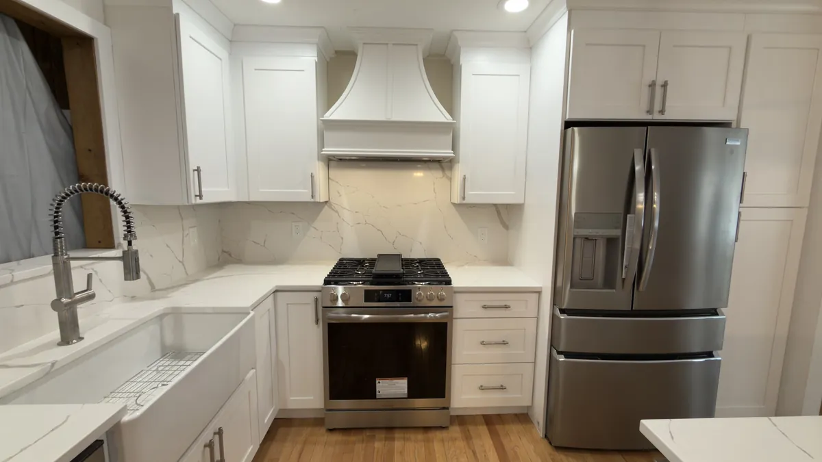 White shaker kitchen with a farmhouse sink, gas range, custom range hood and full-height quartz backsplash