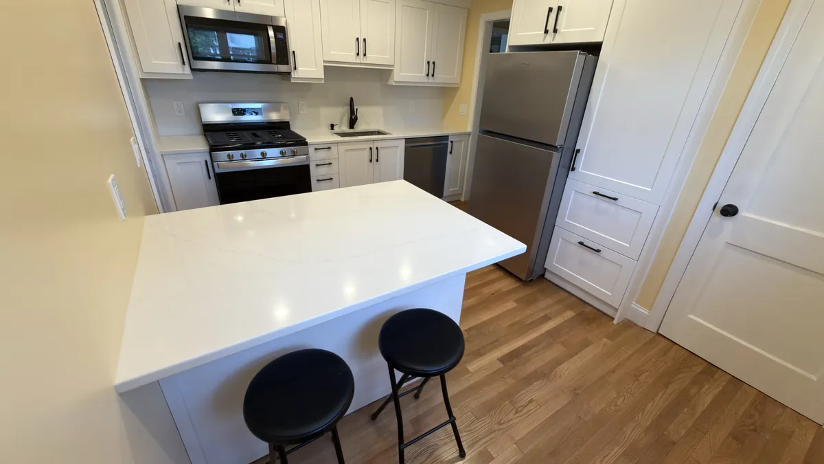 White shaker kitchen with a quartz island, bar stools, gas range and hardwood floor